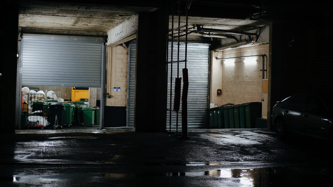 Dark industrial garage at night with open doors showing bins and equipment.