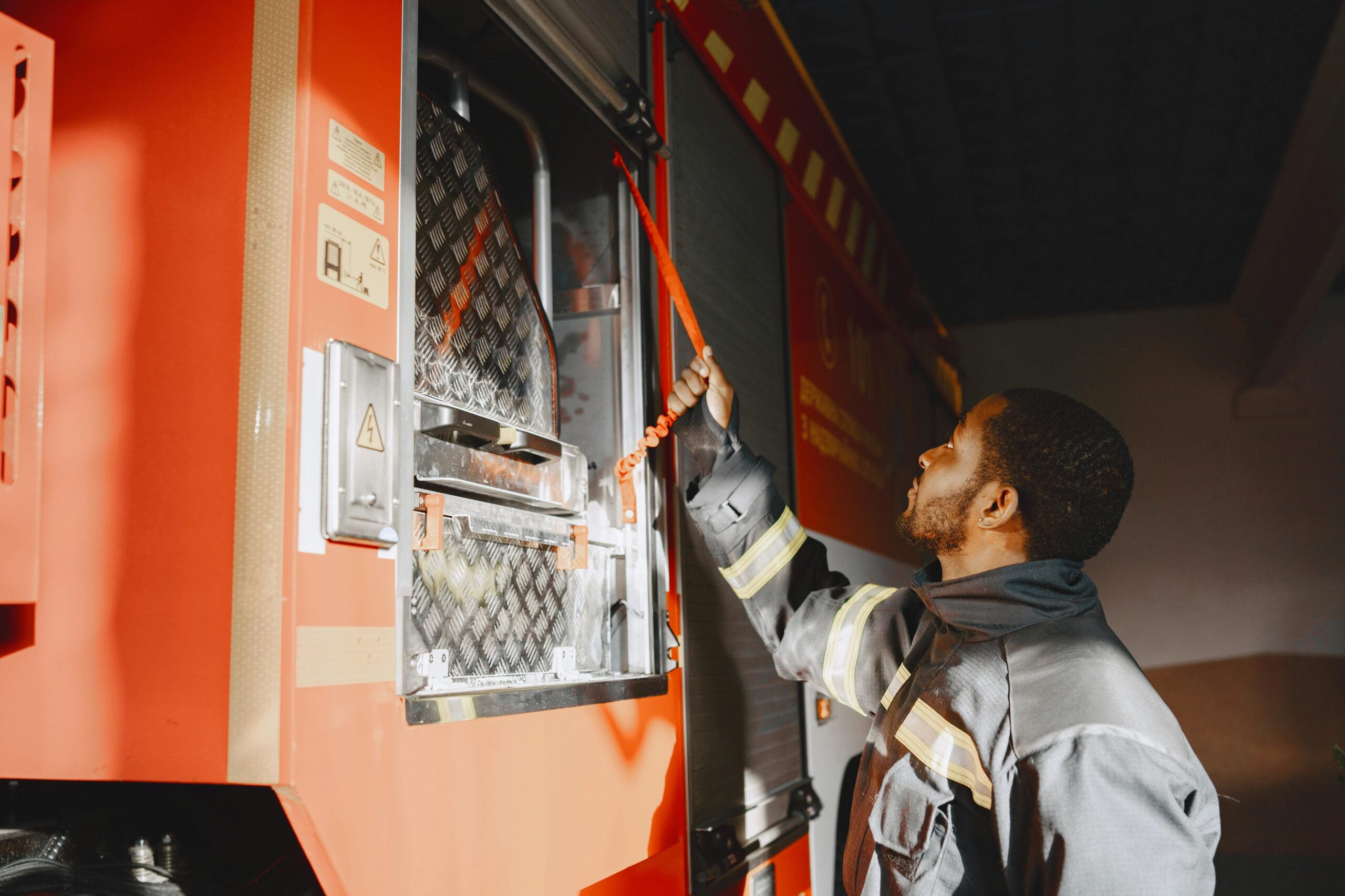 Firefighter in protective clothing securing equipment on a red firetruck in a garage.